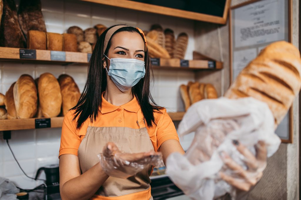 Padeiro de avental no balcao da padaria independente atendendo cliente com bandeja de pao fresco